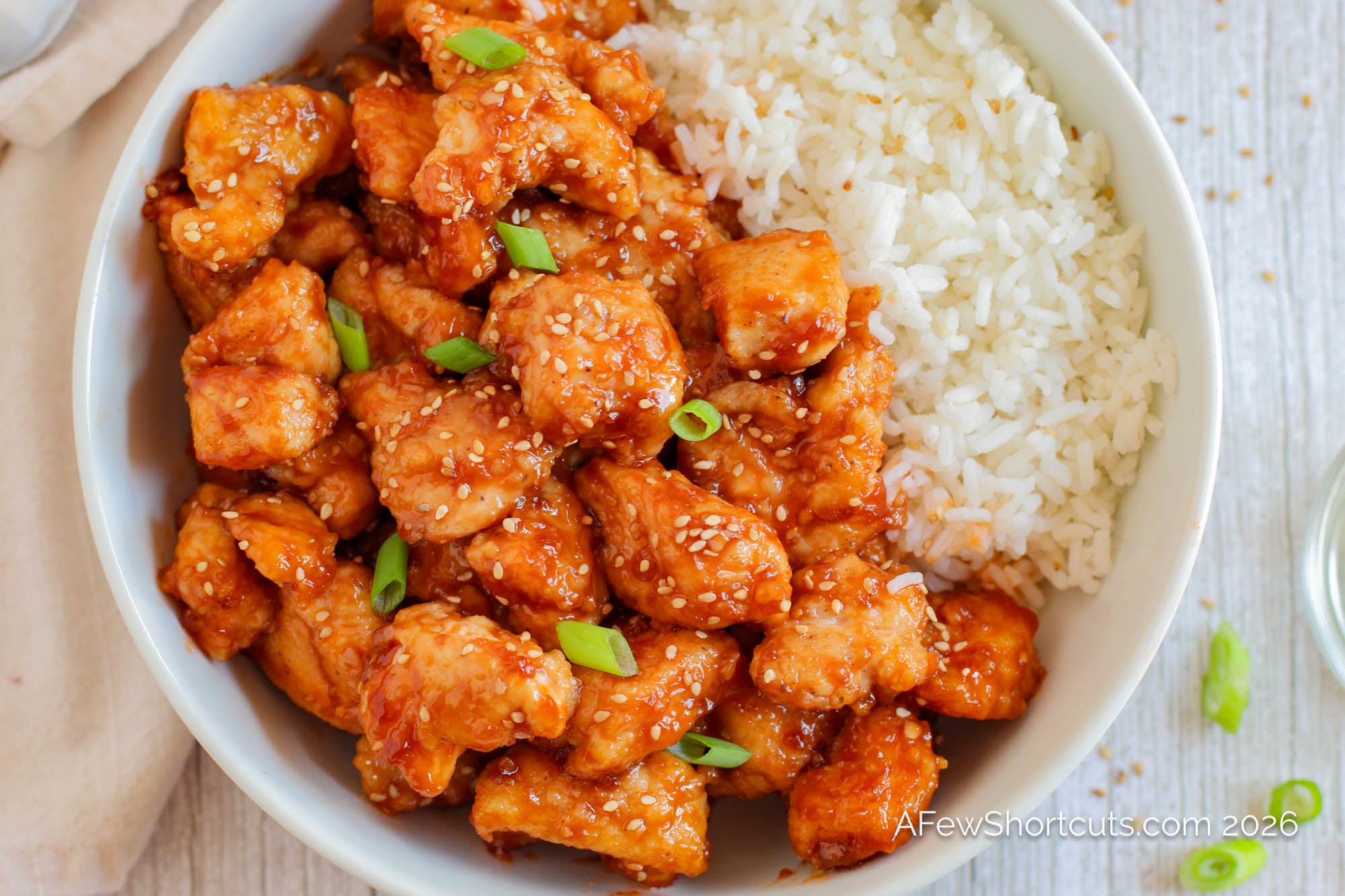 sticky sesame chicken in bowl with rice and scallions